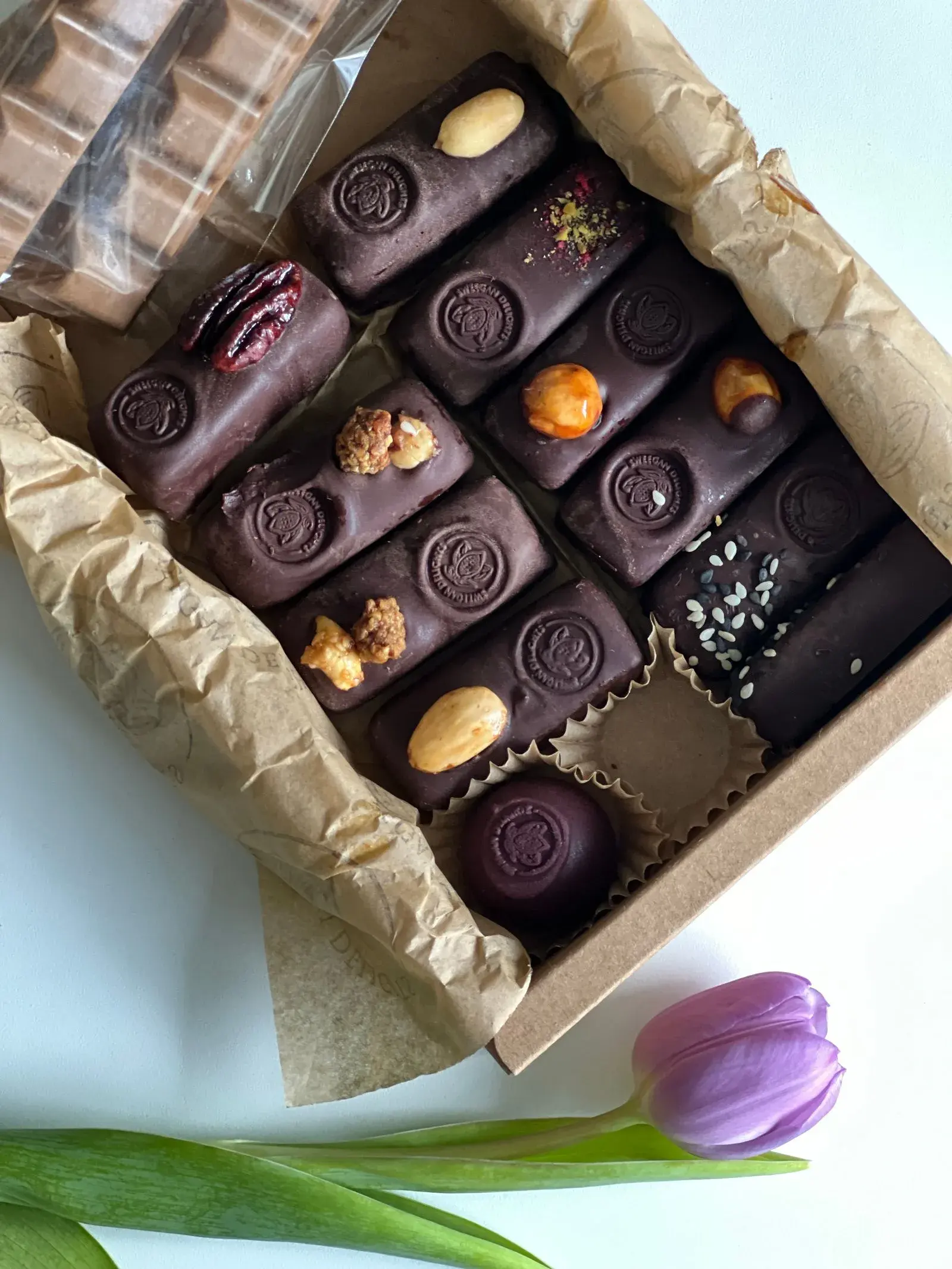 An open kraft box of chocolates beside a tulip