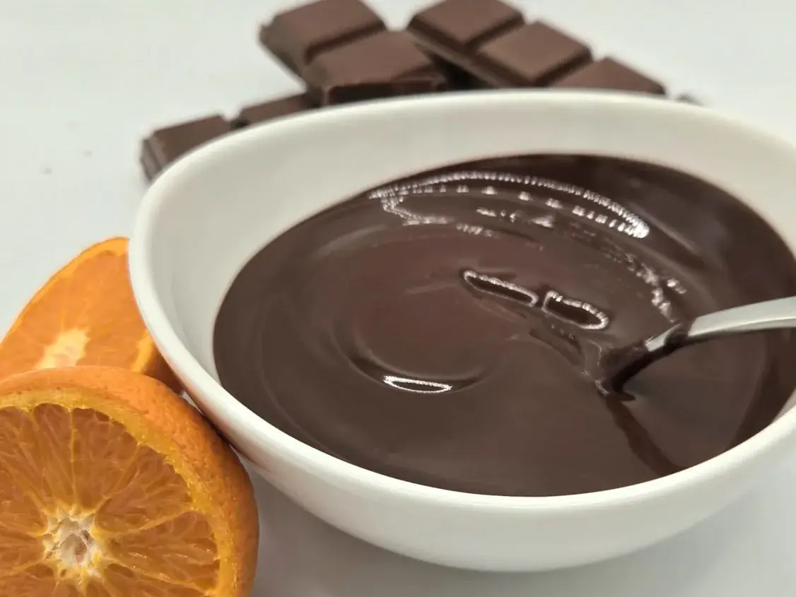 A bowl of melted chocolate beside a halved tangerine